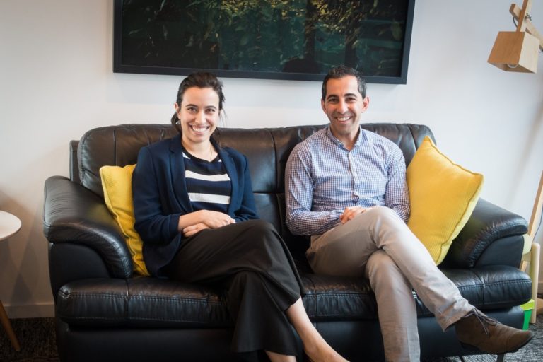 Dr. Azza Al-Ani and Dr. Mo Al-Dujaili smile while seated on a couch.